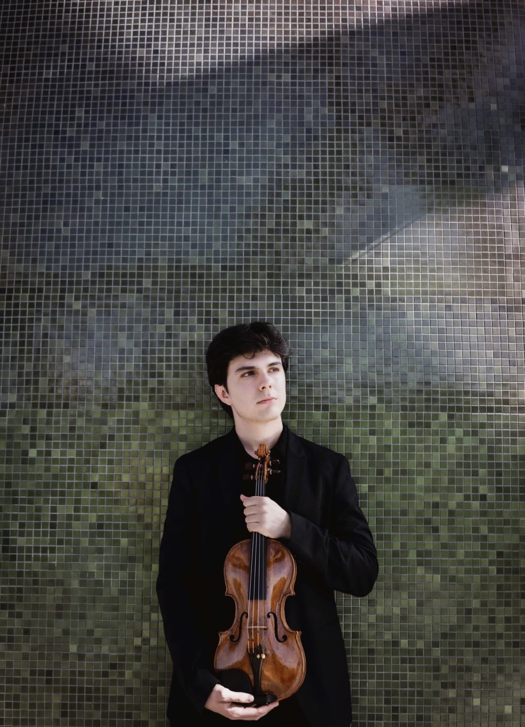 Portrait de Gabriel Rostagni debout avec son violon devant une mosaïque